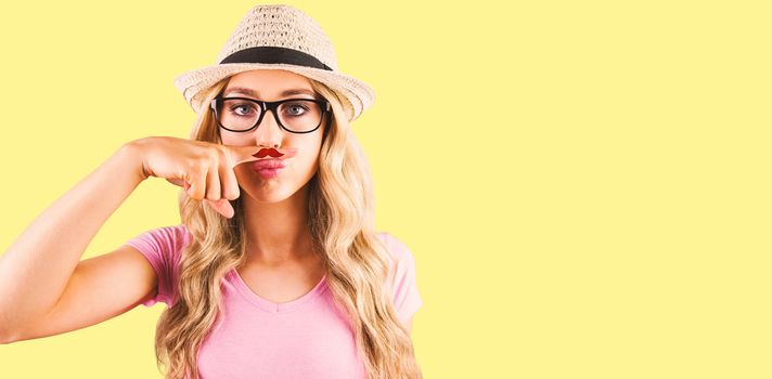 A beautiful hipster having a fake distinguished mustache  against yellow background