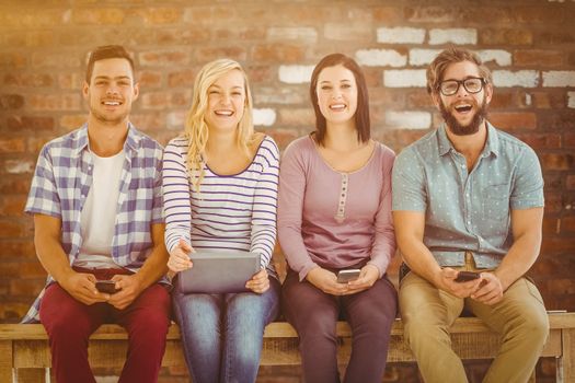 Portrait of smiling business people holding electronic gadgets  against brick wall