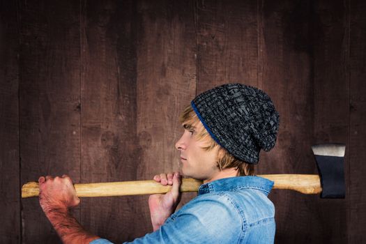 Side view of hipster standing with axe against weathered oak floor boards background