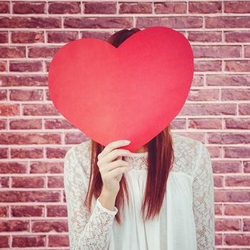 Smiling hipster woman behind a big red heart against red brick wall