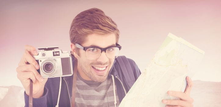 Portrait of happy man holding map and camera against mountain trail