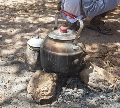 Traditional kettle on camp fire in desert with local bedouin man
