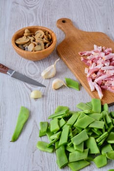 Mushrooms, sliced bacon and cut green peas on wooden table