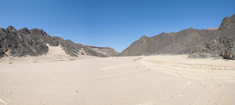 View down a dry wadi desert river valley in barren arid climate with mountains