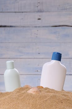 Two bottles of sun lotion and seashells in sand against of blue wooden wall