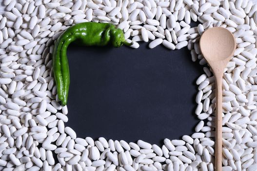 Green pepper, spoon and white kidney beans on blue background.Copy space,from above