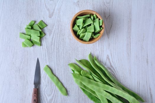 View on cut green peas with knife and bowl on wooden table. From above