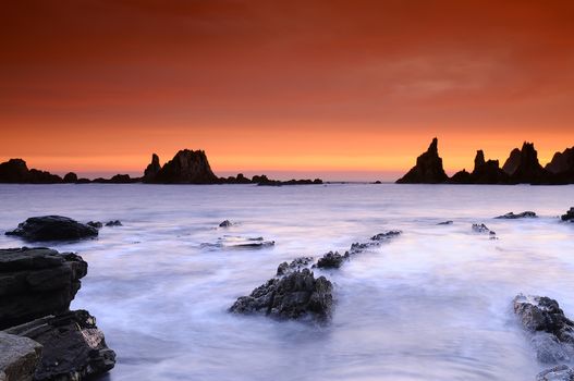 Beautiful rocky shoreline against of bright orange sky at sunset. Long exposure.