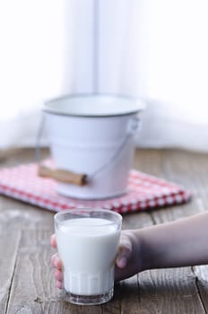 Unrecognizable kid holding glass of fresh tasty milk. Bucket on background.