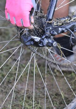 Unrecognizable woman in pink glove fixing dirty bicycle chain in close-up