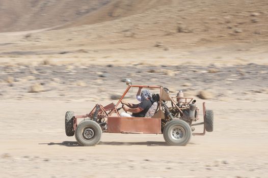 Man in a dune buggy racing across desert landscape at speed with motion blur