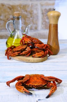 Red boiled crab on table with stack of crabs on wooden board with pepper and olive oil