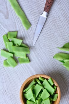 View on cut green peas with knife and bowl on wooden table. From above