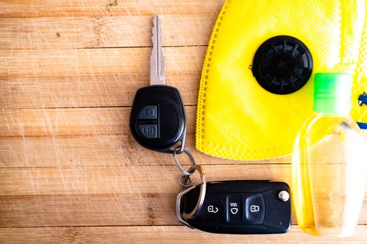 Car keys, sanitizer, yellow mask and more placed on a wooden board with the new essentials for going outdoor with the coronavirus covid 19. Shows necessary safety items for going to office, going shopping to market and more with the new normal