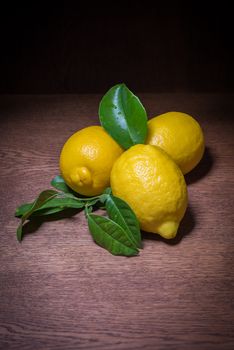 Still life of lemons with their leaves and on wooden table