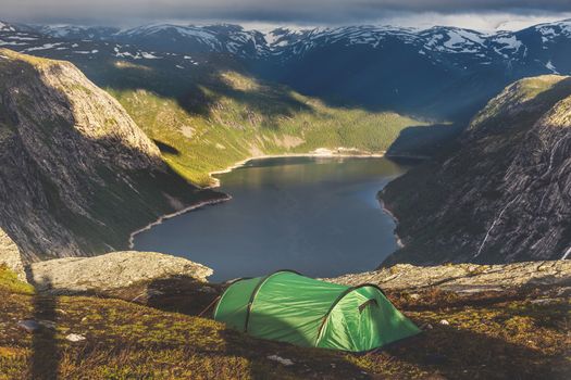 Tourist's tent stands in the mountains near famous landmark - Troll tongue rock or Trolltunga. Sunrise above beautiful fjord in Norway.