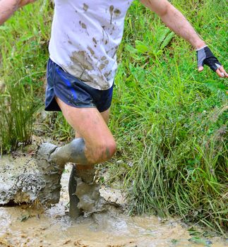 Unrecognizable man in dirty clothes running in mud