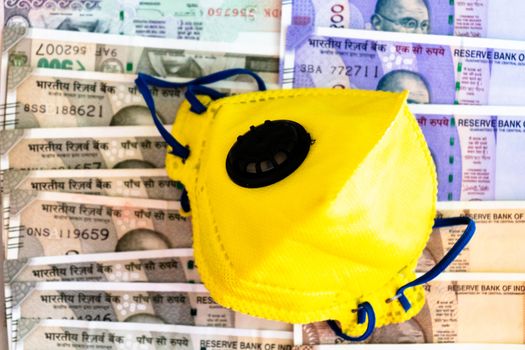 Safety and business essentials yellow mask and sanitizer placed on bed of indian currency. Showing the high price, essentials, large business of manufacturing personal protective essentials or value of health concept