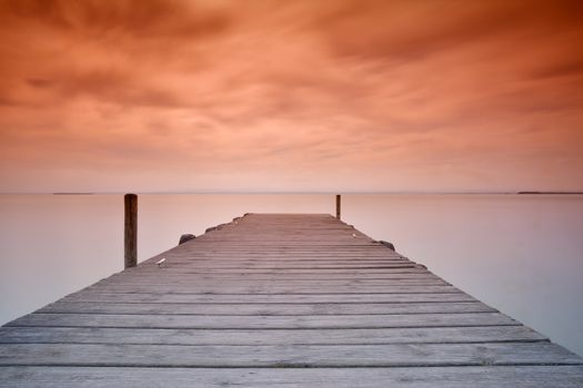 View on scenic seascape with wooden pier at sunset of red and orange colors