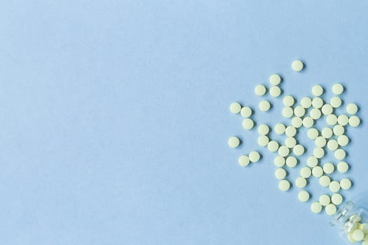 yellow tablets on a pastel blue background. Tablets and a glass bottle on a blue background. Medicine, healthcare and tablets concept. Flatley. The view from the top. copyspace for text.