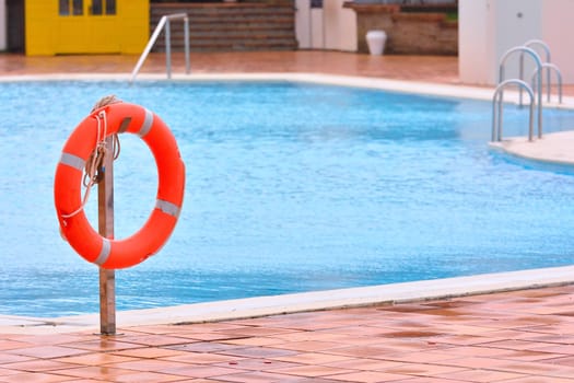 Orange life buoy hanging near swimming pool on metal bar