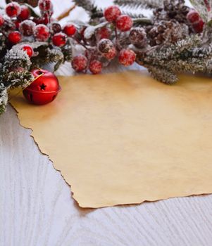 Close-up of brown wrapping paper on wooden table with snowed faux fir-tree branch with christmas ball and berries