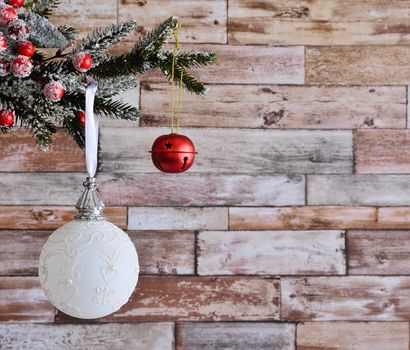 Close up of white Christmas ball at left side hanging on decorative fir branch against of wooden wall