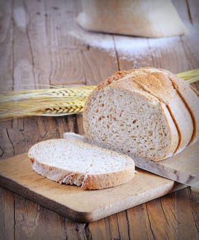 Close-up of cut white bread on wooden board. Oats on background.