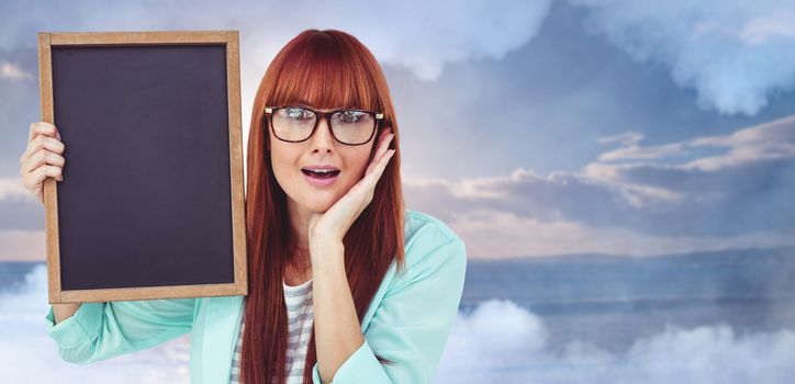 Smiling hipster woman holding blackboard against scenic view of sea against sky