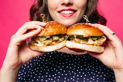 Close-up of unrecognizable brunette smiling woman holding two delicious fresh burgers with juicy roasted chicken and rocket salad.