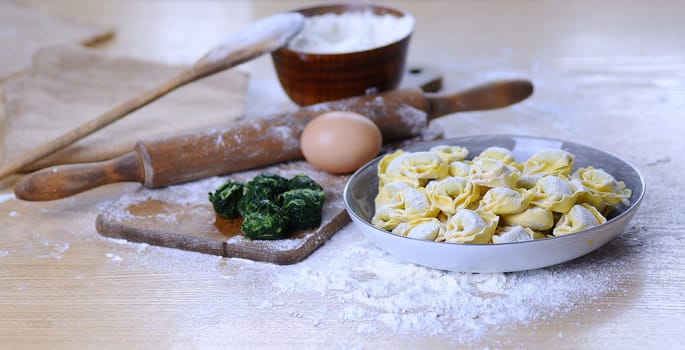 Preparing homemade tortellini on wooden table in the kitchen.