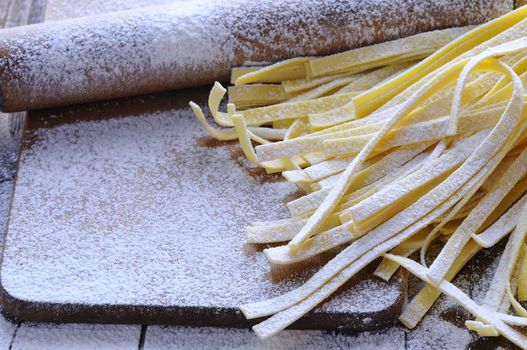 Uncooked spaghetti and rolling pin on board covered with flour