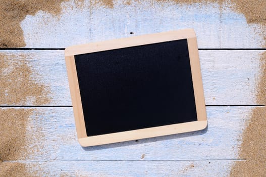Blackboard and blue wooden table on beach sand.