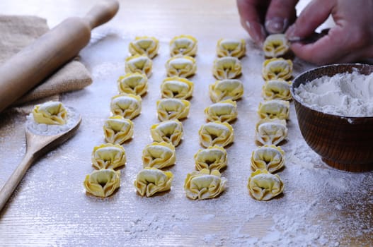 Preparing homemade tortellini on wooden table in the kitchen.