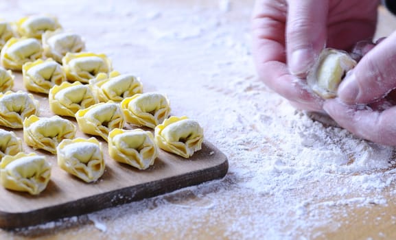 Preparing homemade tortellini on wooden table in the kitchen.