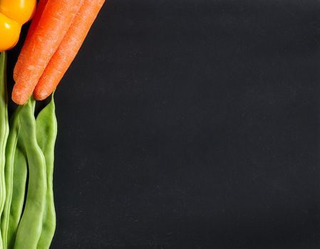 Fresh vegetables as carrots, beans and peppers on a blackboard.