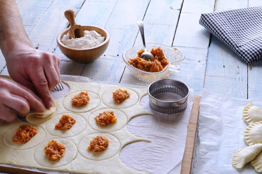 Man's hands making dumplings on wooden board. Unrecognizable