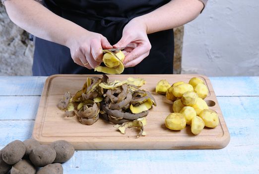 Peeling potatoes on wooden table in the kitchen.