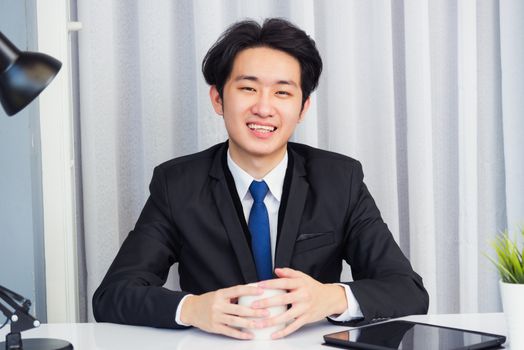 Work from home, Asian young businessman video conference call or facetime he smiling looking to camera sitting with hands on desk using smart digital tablet computer at home office