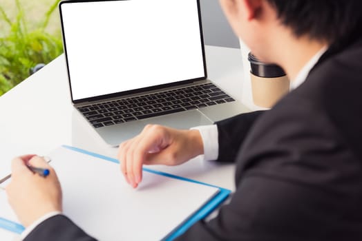 Work from home, Asian young businessman smile wearing suit video conference call or facetime by laptop computer on desk and write taking notes on paper at home office