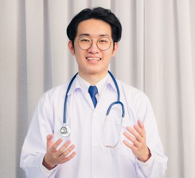 Portrait of Happy Asian young doctor handsome man smiling in uniform with stethoscope talking online video conference call or facetime raise his hand to explain, healthcare medicine concept