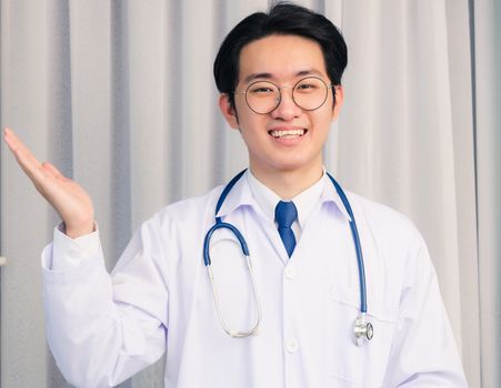 Portrait closeup of Happy Asian young doctor handsome man smiling in uniform and stethoscope neck strap show up hands and looking to the camera with copy space, healthcare medicine concept