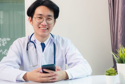 Asian doctor young handsome man smiling using working or holding with digital smart mobile phone at hospital desk office, Technology healthcare medical concept