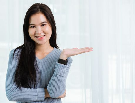 Close up headshot portrait young Asian happy beautiful woman healthy smiling face long hair stand showing something on hand side away space, studio shot looking to camera at home and have a copy space