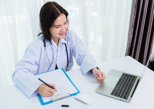 Asian doctor young beautiful woman smiling using working with a laptop computer and her writing something on paperwork or clipboard white paper at hospital desk office, Healthcare medical concept