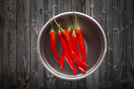 Fresh red chilli pepper in water on bowl of steel on dark wooden background,copy space, Overhead view of chili pepper on wood background
