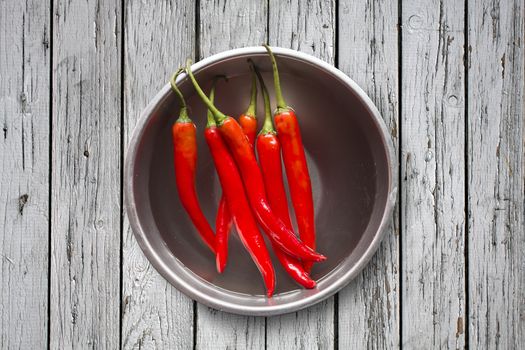 Fresh red chilli pepper in water on bowl of steel on grey wooden background,copy space, Overhead view of chili pepper on wood background