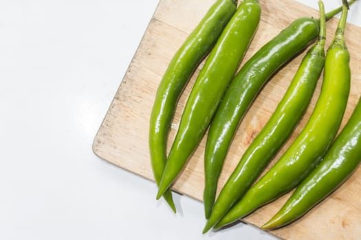  green chilies on a wooden cutting board.