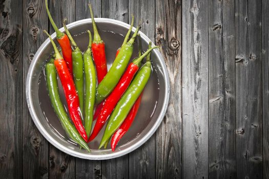 Red and green chilli pepper in water on bowl of steel on black wooden  background,top view