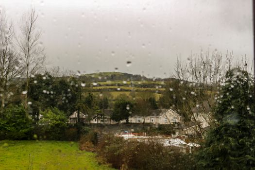 VIEW OF MOUNTAINS OUTSIDE OF DUBLIN IRELAND WITH WATER DROPLETS ON THE GLASS ON A RAINY DAY. TYPICAL IRISH WEATHER DURING FEBRUARY, THE MOUNTAIN SIDE IS ICONIC OF IRELAND